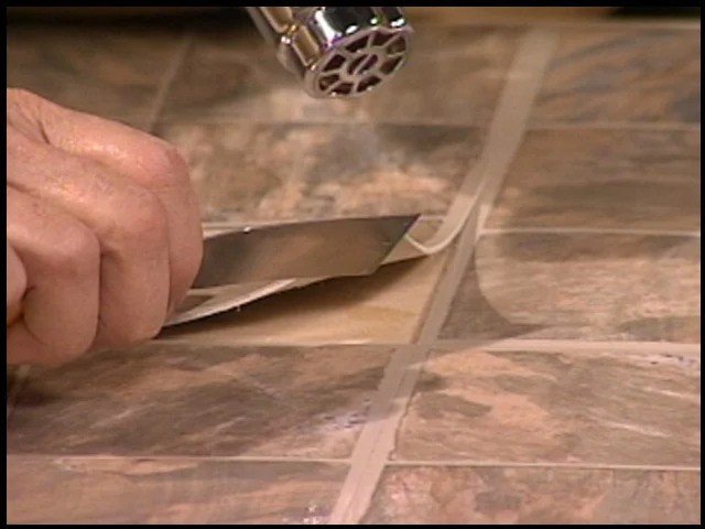 Using a heat tool and putty knife to fix a lifted peel and stick tile edge. 