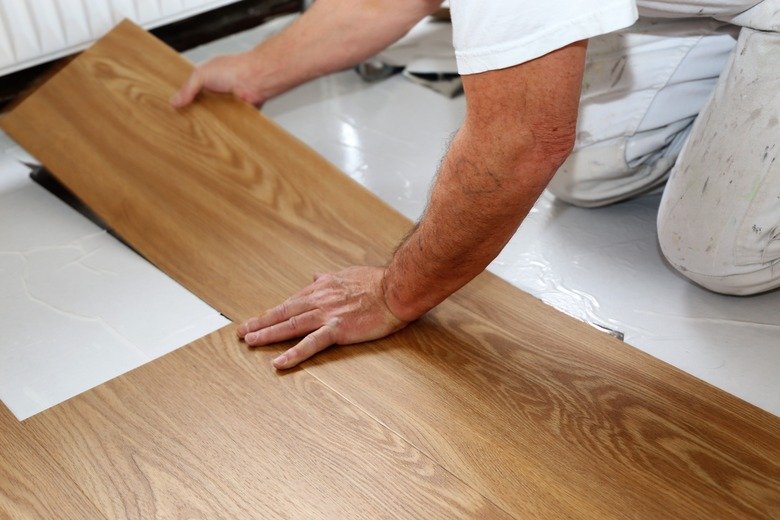 A homeowner installing wood-look peel and stick floor tiles during a DIY flooring project.