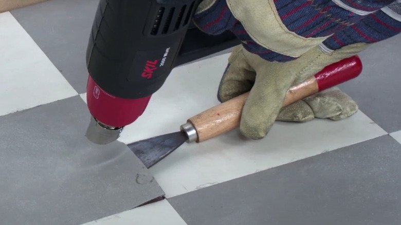 Person removing a floor tile with a scraper after a flooring installation mistake.